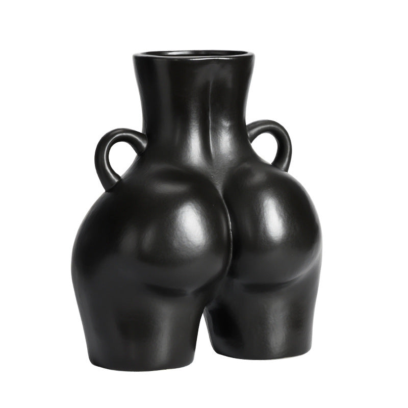 A black ceramic gourd-shaped vase on a white surface, with a bouquet of multicolored flowers arranged in it, placed against a neutral background with a grey sofa.