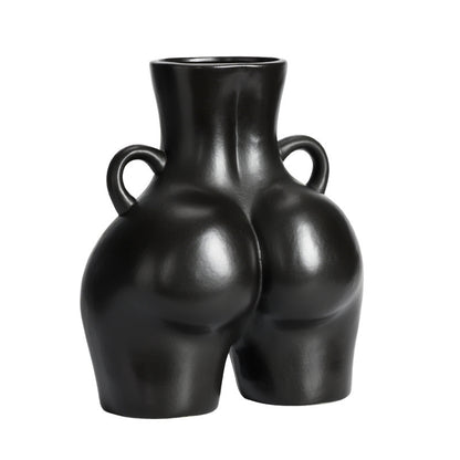 A black ceramic gourd-shaped vase on a white surface, with a bouquet of multicolored flowers arranged in it, placed against a neutral background with a grey sofa.