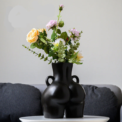 A black ceramic gourd-shaped vase on a white surface, with a bouquet of multicolored flowers arranged in it, placed against a neutral background with a grey sofa.
