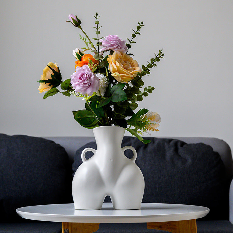 White abstract vase with colorful flowers on a table against a gray wall.