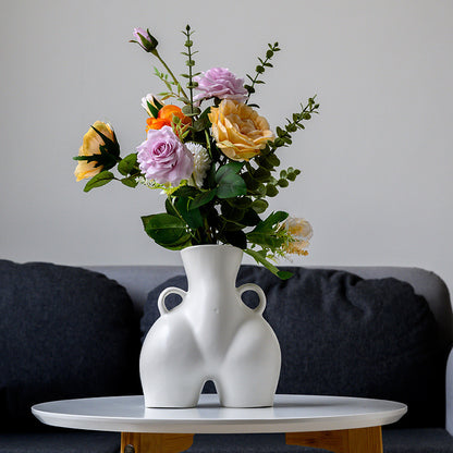 White abstract vase with colorful flowers on a table against a gray wall.