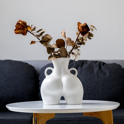 White vase with dried flowers on a table against a gray wall