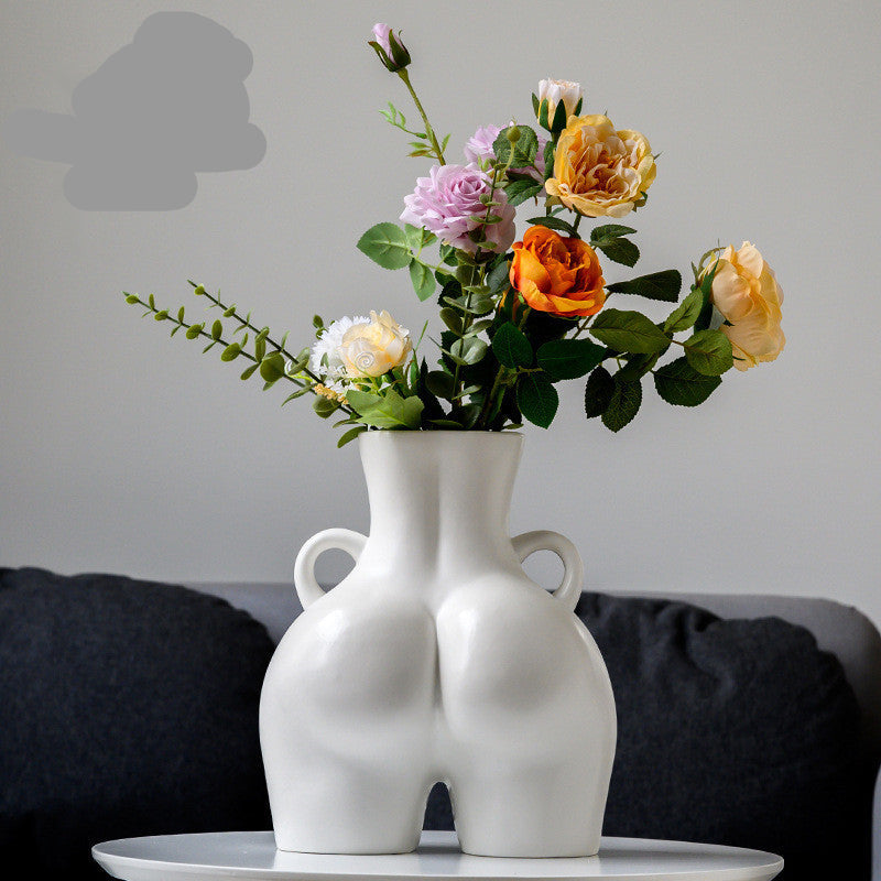 A black ceramic gourd-shaped vase on a white surface, with a bouquet of multicolored flowers arranged in it, placed against a neutral background with a grey sofa.