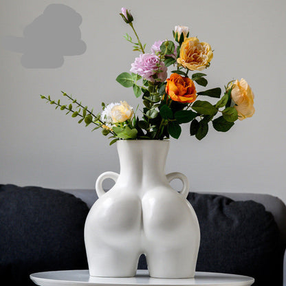 A black ceramic gourd-shaped vase on a white surface, with a bouquet of multicolored flowers arranged in it, placed against a neutral background with a grey sofa.