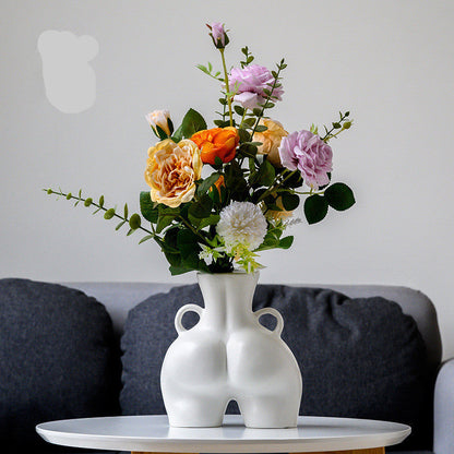 A black ceramic gourd-shaped vase on a white surface, with a bouquet of multicolored flowers arranged in it, placed against a neutral background with a grey sofa.