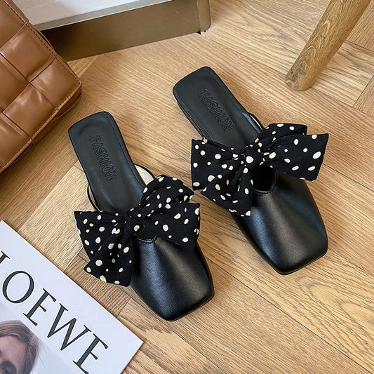 Black slides with polka dot bows on a wooden floor