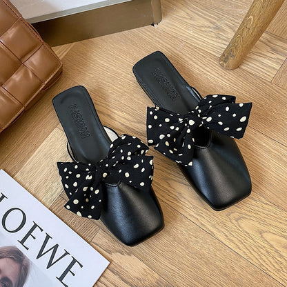 Black slides with polka dot bows on a wooden floor