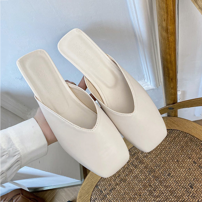 Beige mules worn by a person sitting on a wooden chair.