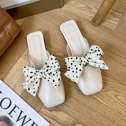 White sandals with polka dot bows on a wooden floor