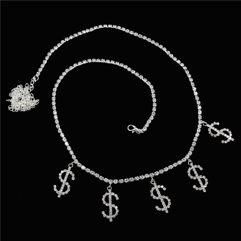 A gold-colored metal belly chain with rhinestone mosaic details, featuring small dollar sign charms, worn on a black bikini bottom.