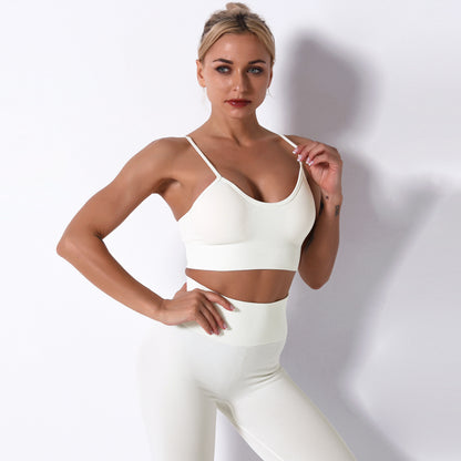 Woman wearing a white sports bra and leggings against a plain background