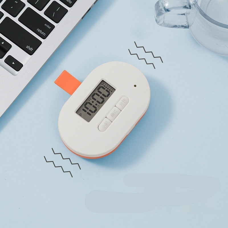 White and orange digital device with a screen and buttons on a light blue surface with keyboard and glass.