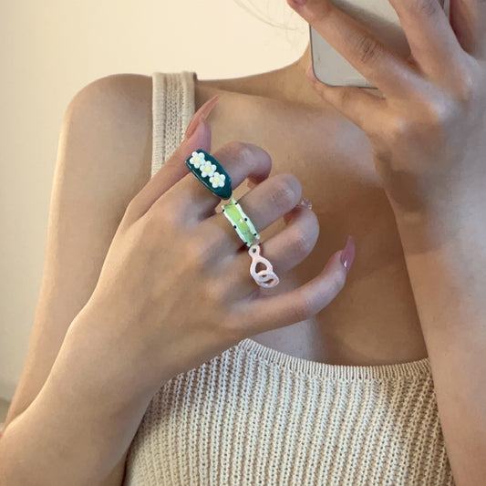 Close-up of a hand wearing multiple rings with floral designs on a neutral background