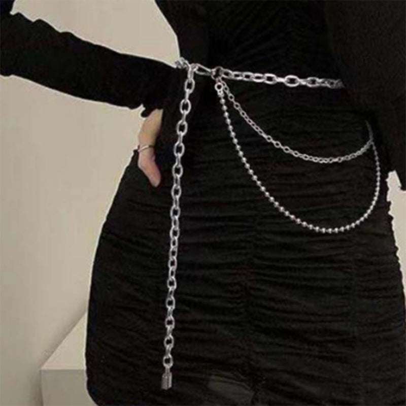 A person wearing a black outfit adorned with a multilayered silver hip hop punk waist chain.