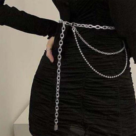 A person wearing a black outfit adorned with a multilayered silver hip hop punk waist chain.