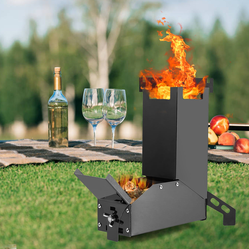 Portable fire pit with flames, wine bottle, glasses, and apples on a grassy outdoor setting.