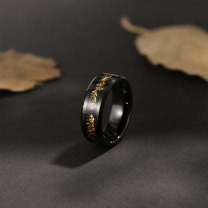 Black ring with gold engraving on a dark surface with leaves