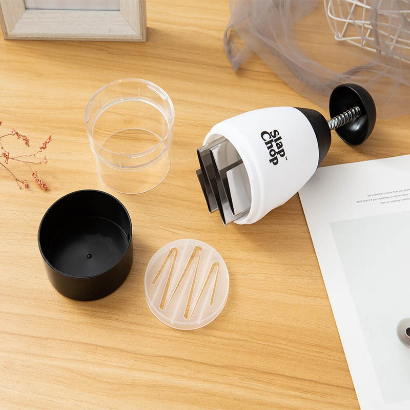 Slap Chop kitchen tool on a wooden surface with a clear plastic cup and black container.