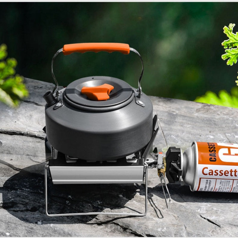 Portable camping stove with a kettle and canister on a wooden surface outdoors.
