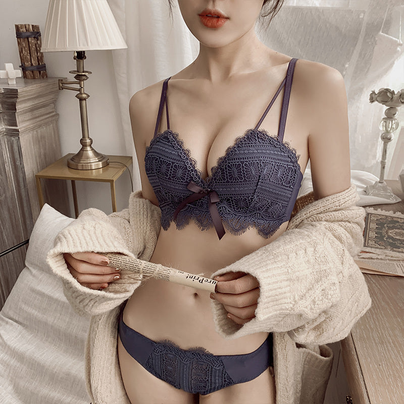 Person wearing a dark blue lace bra and panties set, holding a beige cardigan.