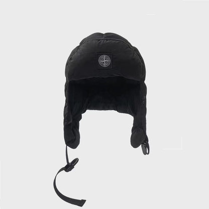 Black winter hat with ear flaps and a brand logo on a light gray background