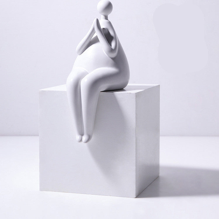 A pair of white ceramic figurines, one sitting and one standing, placed on top of a stack of books with a decorative vase beside them.