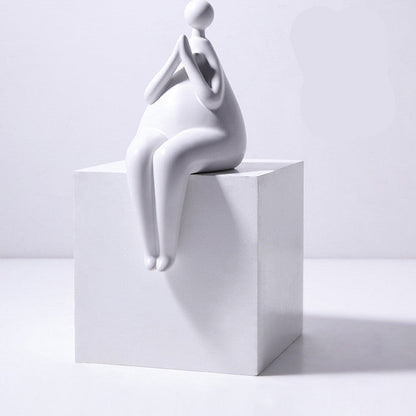 A pair of white ceramic figurines, one sitting and one standing, placed on top of a stack of books with a decorative vase beside them.