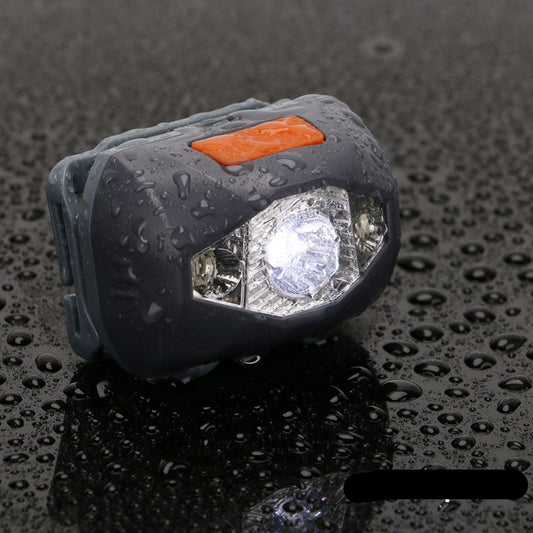 A small, black mini headlight emitting a strong white light, placed on a surface and pointed forward, demonstrating its lighting capability in a dark environment.