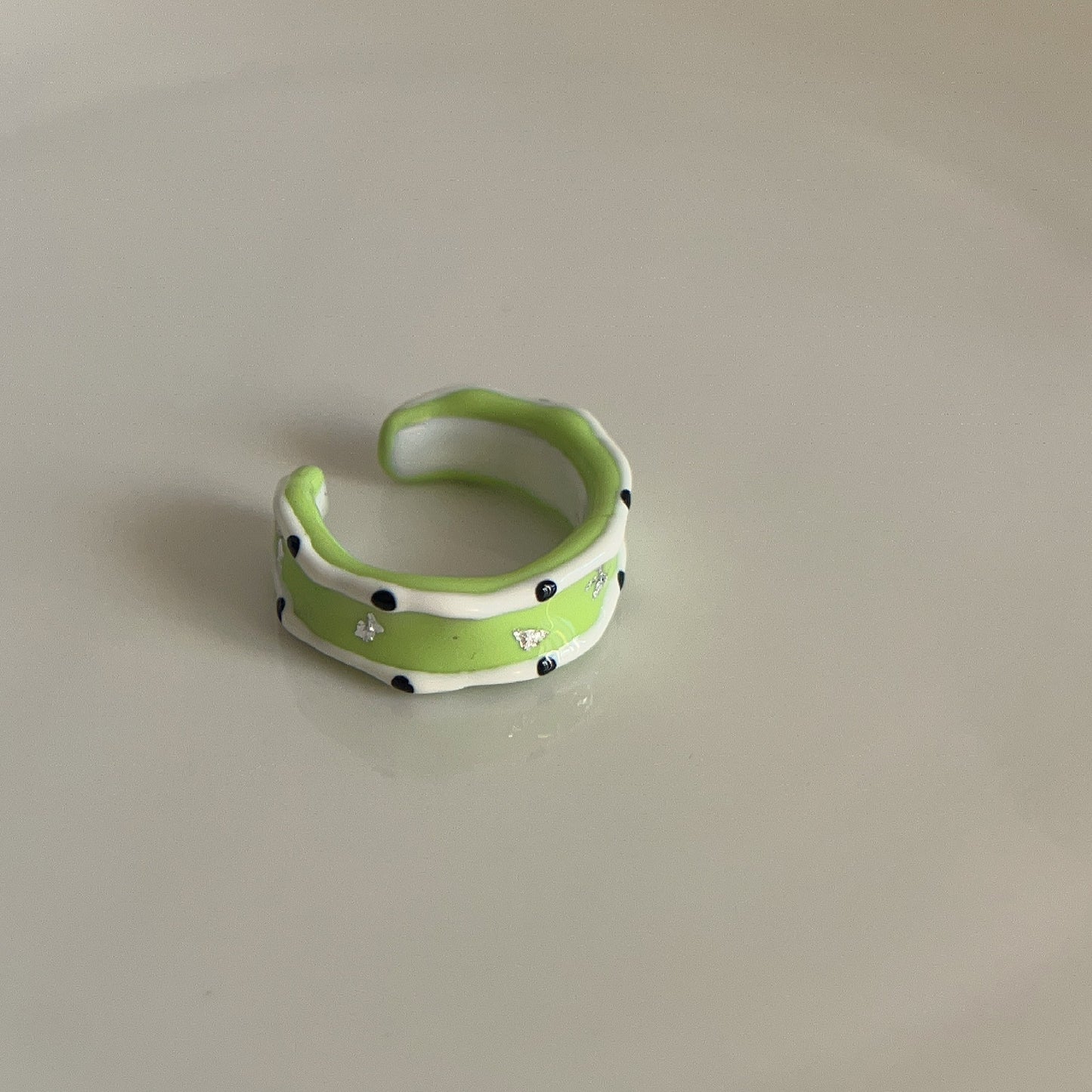 Green ceramic ring with black dots on a beige background