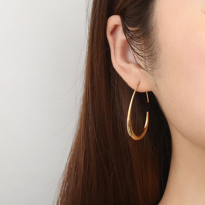 Gold hoop earring worn by a person with long brown hair on a light gray background