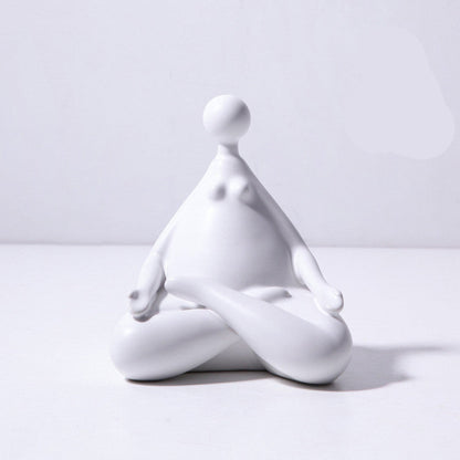 A pair of white ceramic figurines, one sitting and one standing, placed on top of a stack of books with a decorative vase beside them.