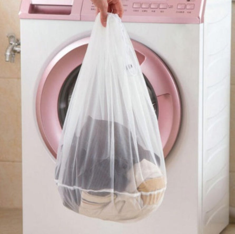 Person holding a white mesh laundry bag with clothes in front of a pink washing machine.