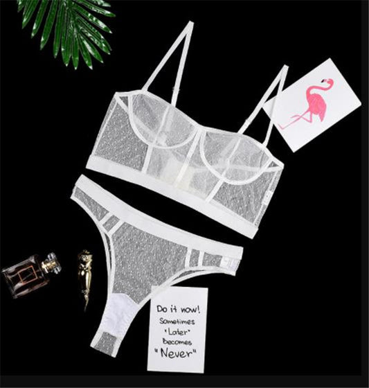 Transparent lingerie set with a perfume bottle and decorative card on a black background