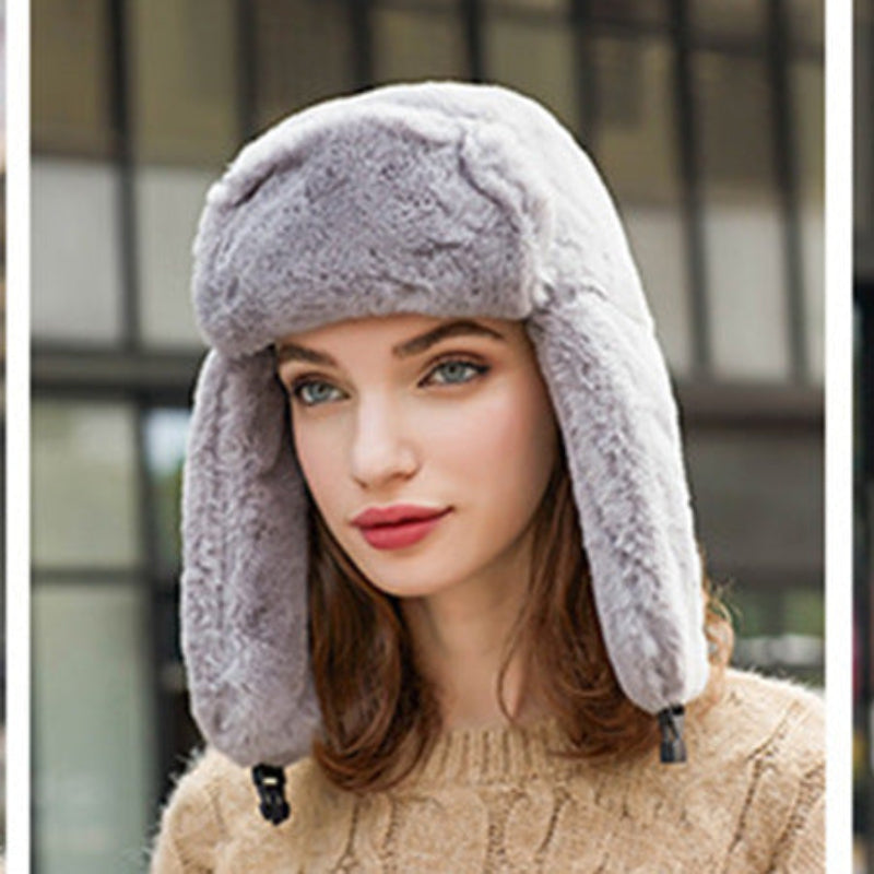 Woman wearing a gray fur-trimmed hat with ear flaps against a blurred background