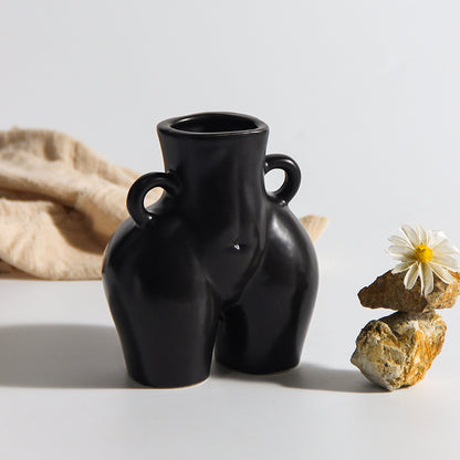 A black ceramic gourd-shaped vase on a white surface, with a bouquet of multicolored flowers arranged in it, placed against a neutral background with a grey sofa.