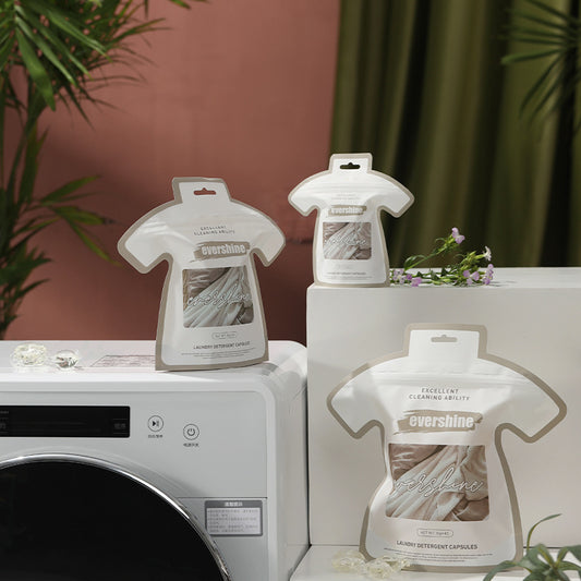 Packaging of laundry gel beads in the shape of a shirt placed on a washing machine, with plants and laundry in the background.