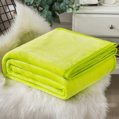 A blue coral fleece blanket placed on a white furry surface, with a part of a bed and a plant in the background.