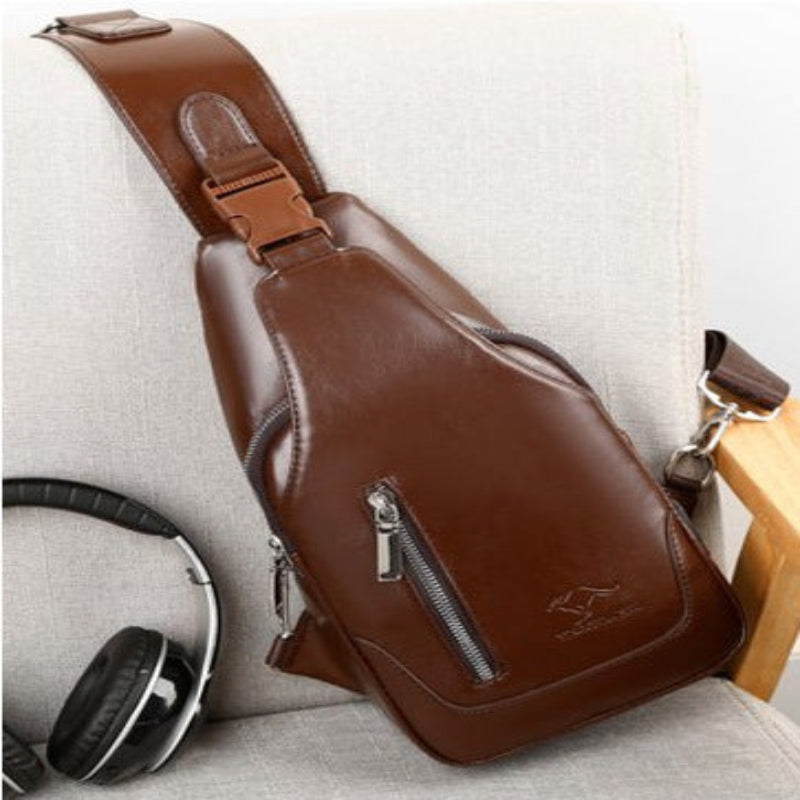 Brown leather sling bag with a zipper on a light gray surface.