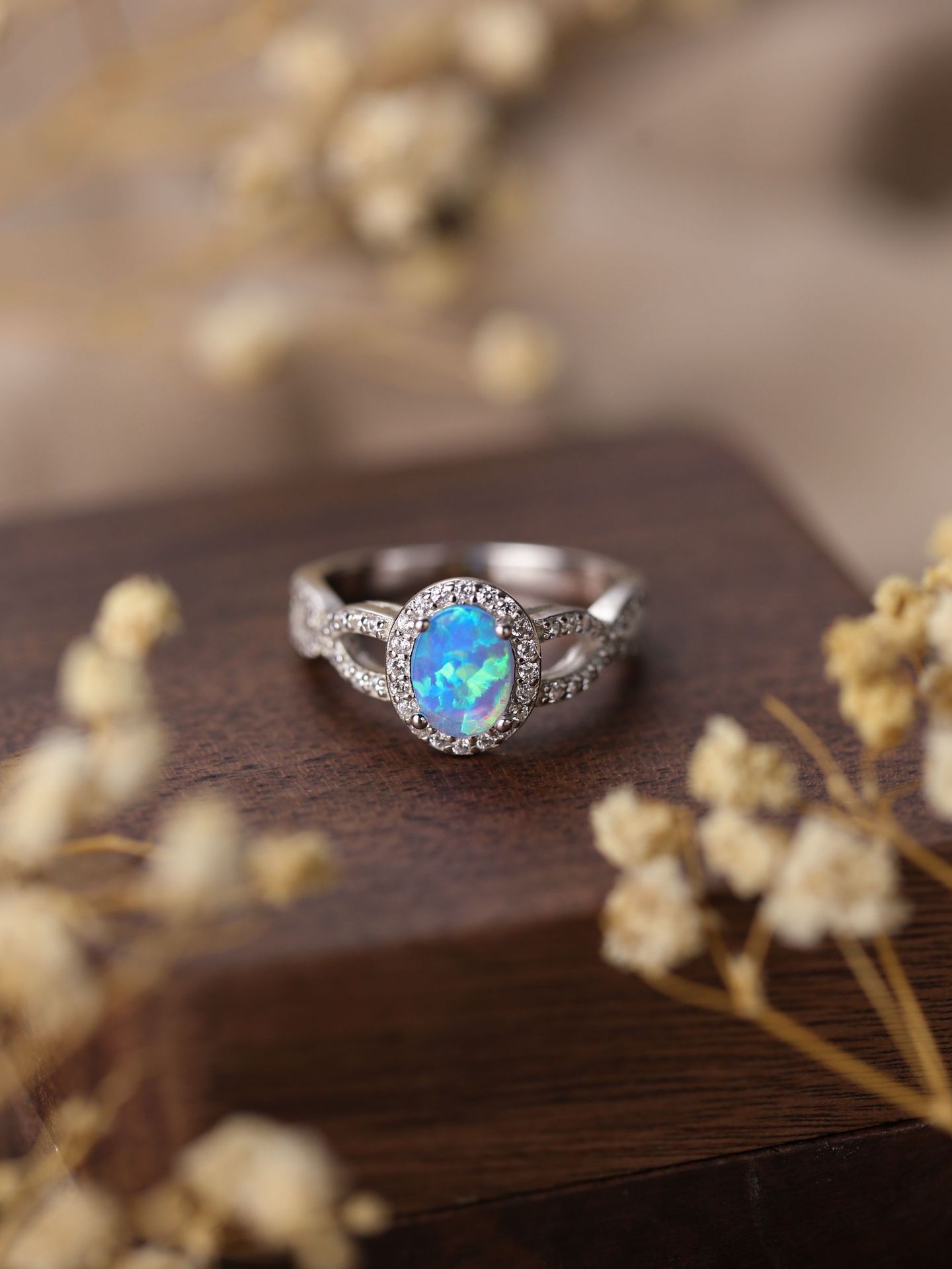 Silver ring with a blue opal stone on a wooden surface with dried flowers.