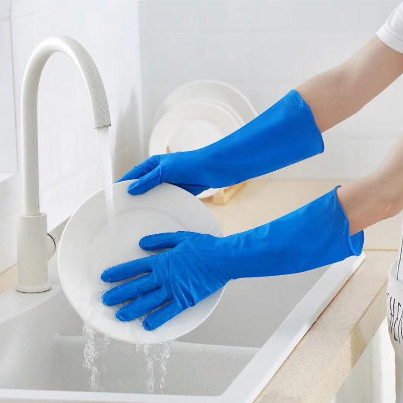 Person wearing blue gloves washing a white plate in a kitchen sink.