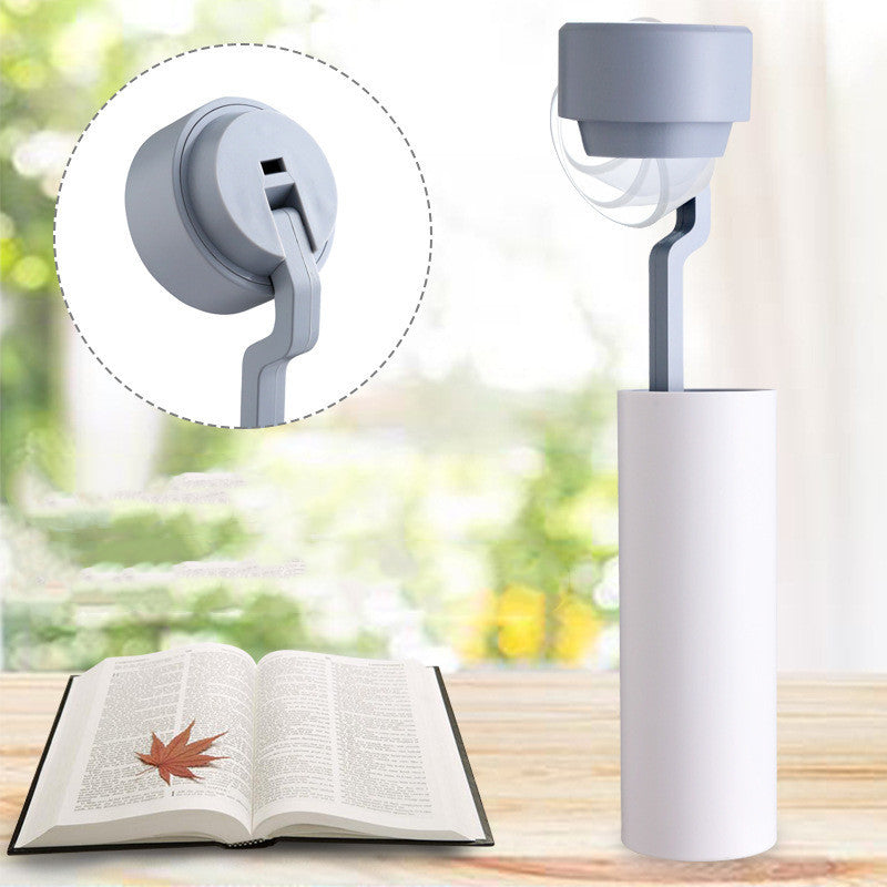 White lamp with flexible neck on a wooden surface next to an open book, with a blurred green outdoor background.