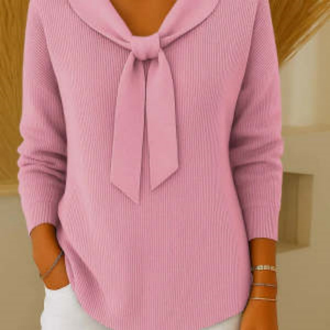 Pink sweater with a tie detail worn by a person, against a neutral background
