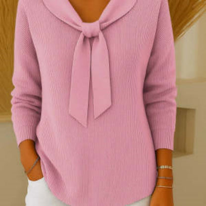 Pink sweater with a tie detail worn by a person, against a neutral background