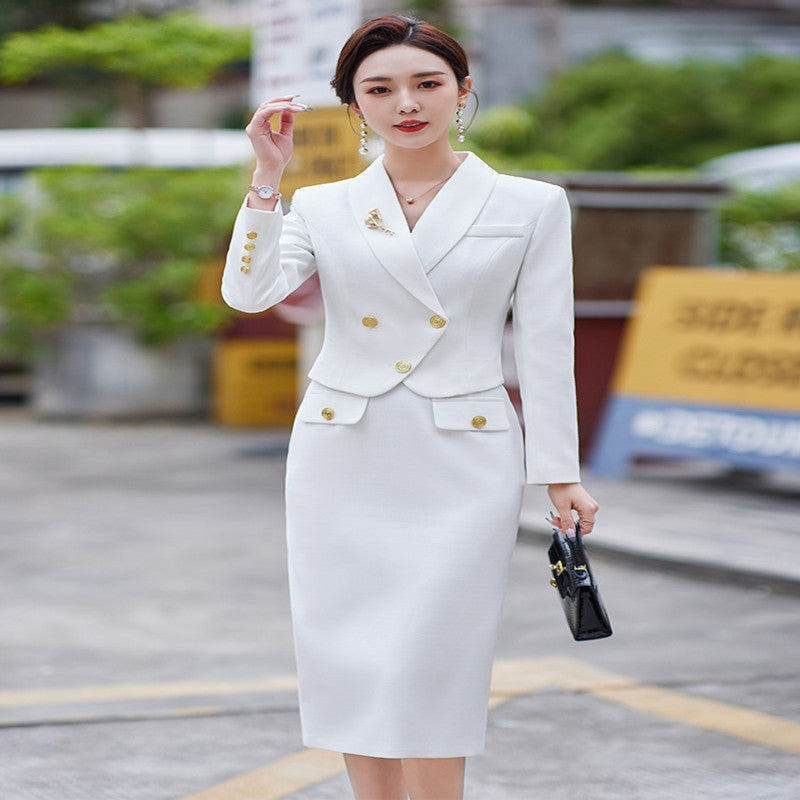 A woman in a white leisure formal suit with a blazer and a skirt, featuring long sleeves and gold buttons, standing outdoors.