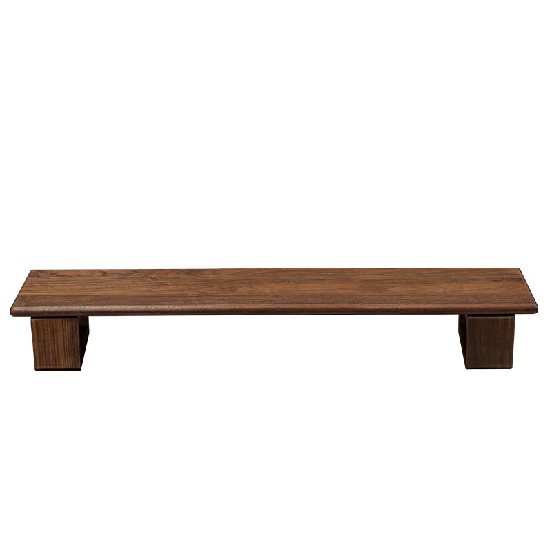 Monitor stand made of black walnut wood, with a computer monitor, keyboard, and various desk accessories on it, placed on a wooden floor against a white background.