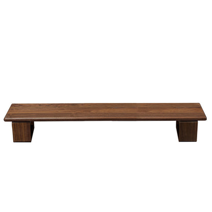 Monitor stand made of black walnut wood, with a computer monitor, keyboard, and various desk accessories on it, placed on a wooden floor against a white background.
