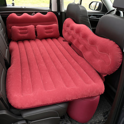 Red inflatable car mattress with attached pillows inside a vehicle.