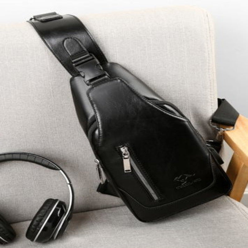 Black leather sling bag on a light gray surface with headphones nearby