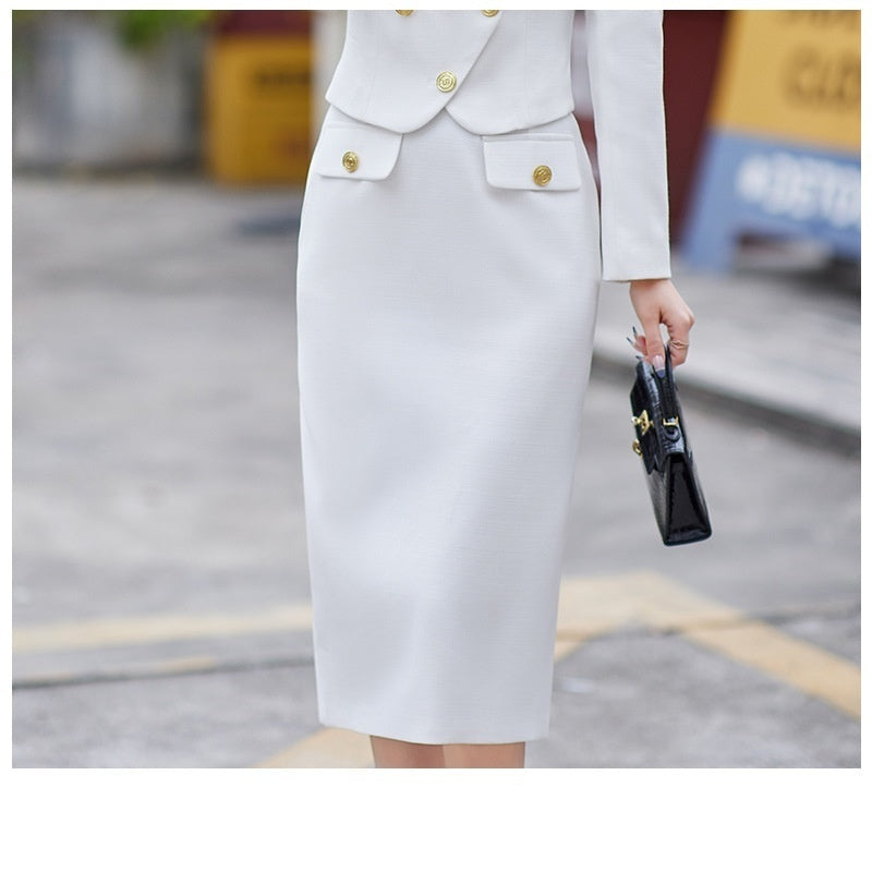 A woman in a white leisure formal suit with a blazer and a skirt, featuring long sleeves and gold buttons, standing outdoors.