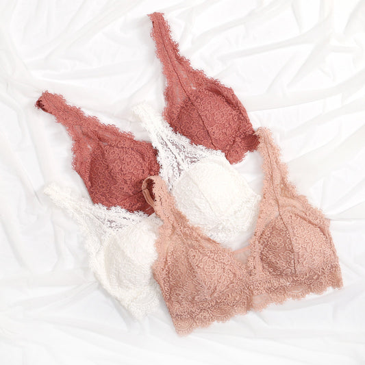 Two lace bras in pink and beige on a white textured surface